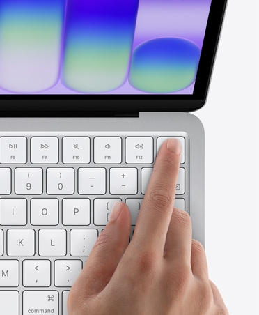 MacBook Neo ezüstszínben, egy ember ujja a billentyűzet jobb felső sarkában található Touch ID érzékelőn.