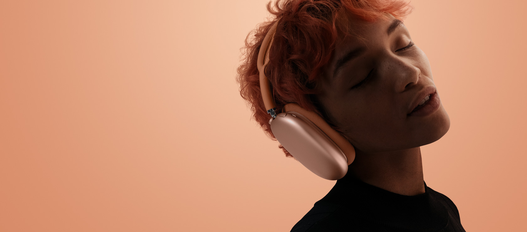 Galvą pakreipęs ir užsimerkęs žmogus su „AirPods Max 2“, oranžinės spalvos, oranžiniame ir rausvame fone