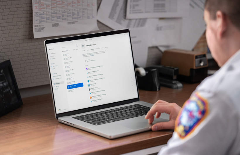 Een brandweercommandant zit in een kantoor en gebruikt een MacBook met Apple Business Essentials geopend op het scherm