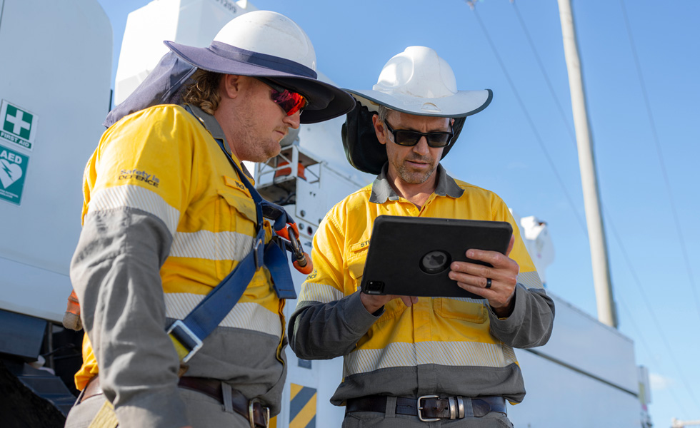 Twee veldwerkers werken samen op een iPad terwijl ze naast een bedrijfswagen staan