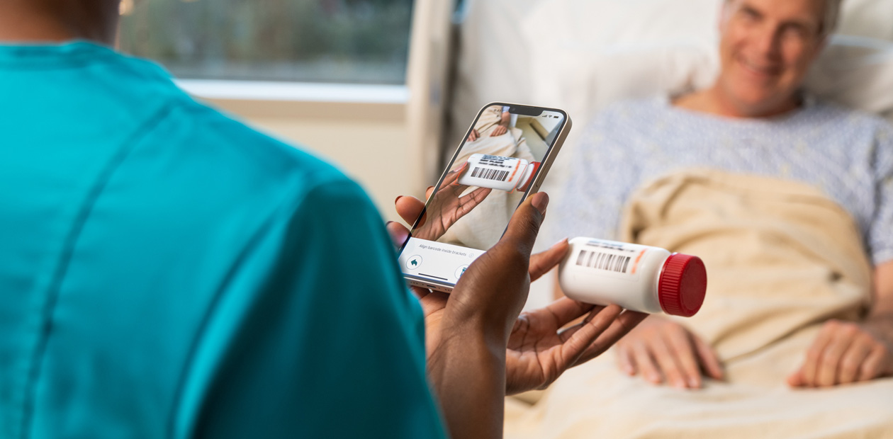 Una enfermera con una bata de color verde azulado escanea el medicamento de su paciente con un iPhone.