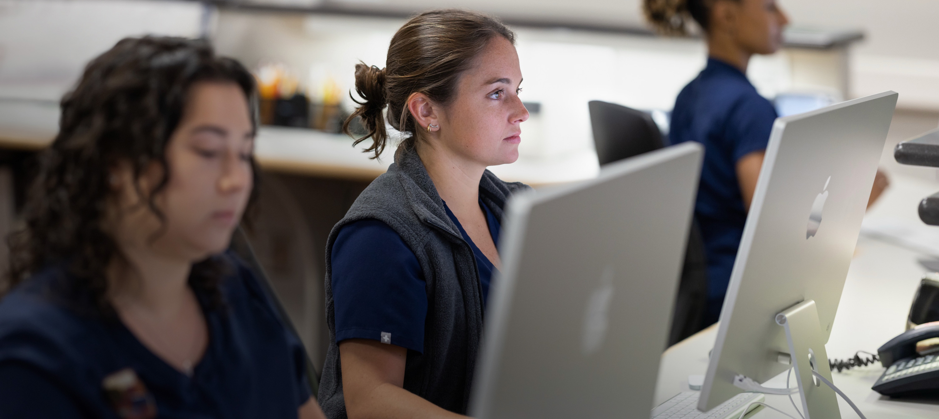 Tre sygeplejersker arbejder bag iMac-skærme.