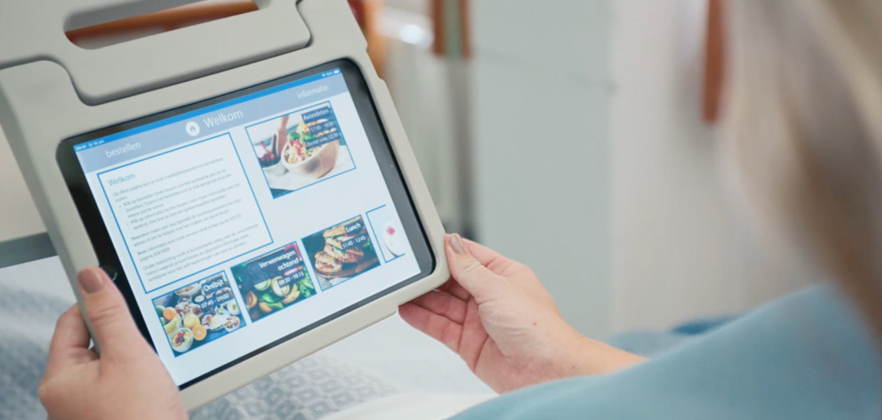 En patient ser på en iPad-skærm, mens hun sidder i en hospitalsseng.