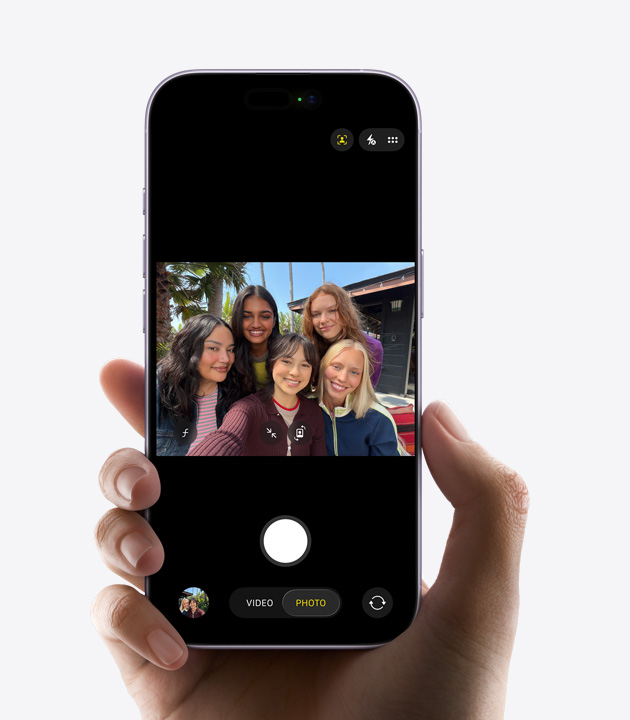 „iPhone“ priekinė dalis, trijų žmonių asmenukės vaizdo įrašo fiksavimas naudojant „Center Stage“ priekinę kamerą, veidus apibrėžiantys geltoni kvadratėliai, kad būtų parodytas automatinis komponavimas