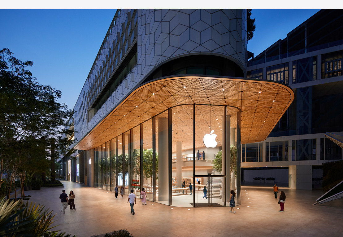 „Apple“ parduotuvė naktį, stikliniai langai, apšviesta viduje, „Apple“ logotipas centre virš pagrindinių durų.
