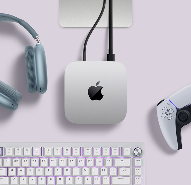 Hõbedase Mac mini pealtvaade, mille tagumised liidesed on ühendatud kahe juhtmega, kõrval on sinised AirPods Max kõrvaklapid, hõbedane Magic Keyboard ja juhtmevaba mängupult
