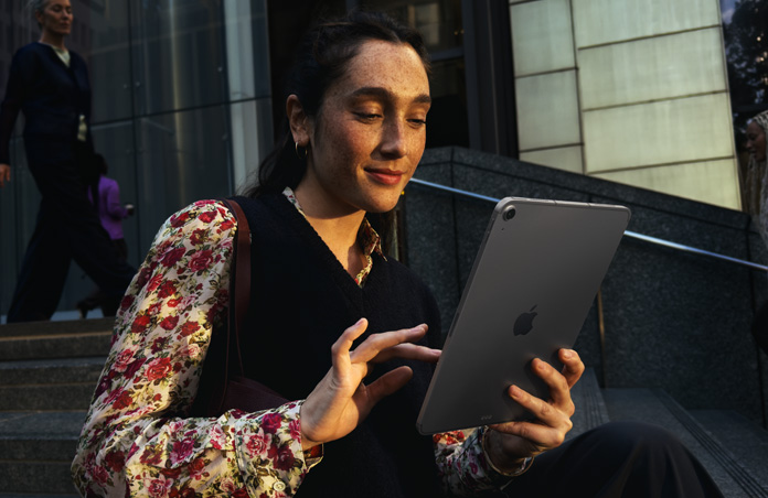 فتاة جالسة على درج خارج مبنى كبير تستخدم جهاز iPad Air مقاس 11 إنش، لون رمادي فلكي، وهي تحظى باتصال سلس ومتواصل عند الانتقال بين شبكة Wi-Fi وأخرى