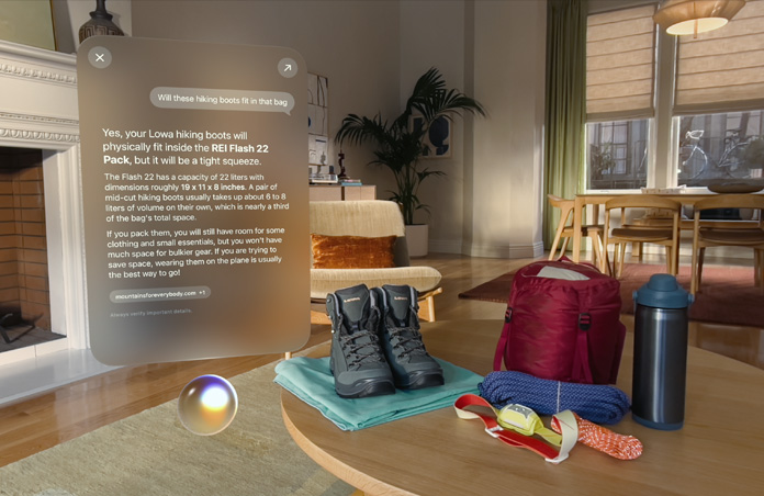 Écran affichant la réponse à une requête Siri sur les essentiels de camping, flottant au-dessus de la sphère Siri sur le côté gauche, avec des chaussures de randonnée, des cordes, un sac à dos, une bouteille d’eau et une lampe frontale posés sur une table sur le côté droit