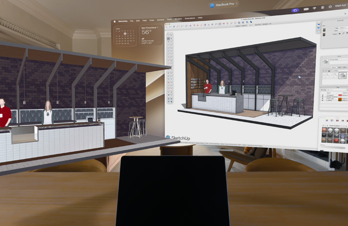 Vue d’un Apple Vision Pro, un MacBook Pro est posé sur une surface avec des modèles 3D projetés à l’arrière ; les modèles représentent un comptoir de café avec deux personnes debout derrière